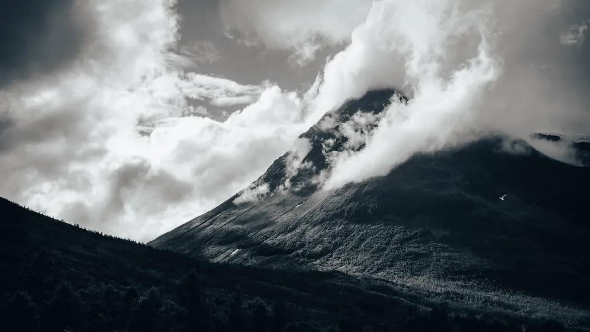 Clouds curl around a dark mountain slope in a black-and-white landscape.