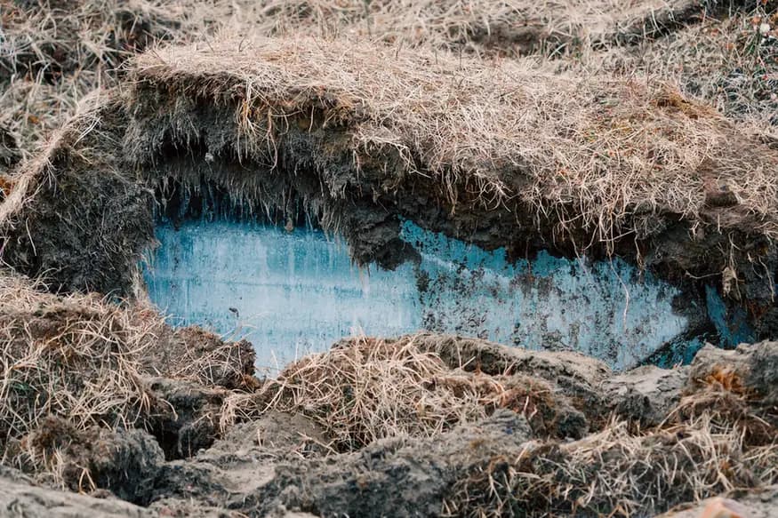 A vivid blue opening of ice beneath grass, roots and rough earth.