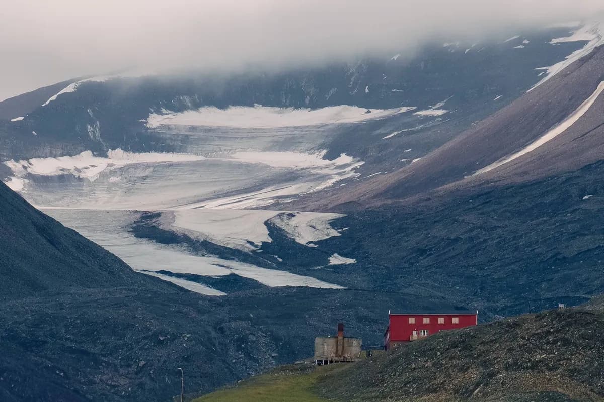 A small red building below a broad grey valley, pale ice and low cloud.
