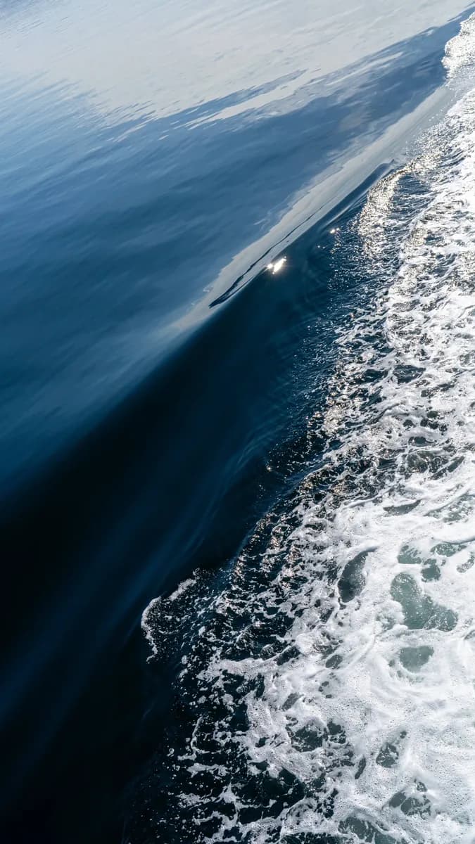 A diagonal wave separating smooth deep blue water from white foam.